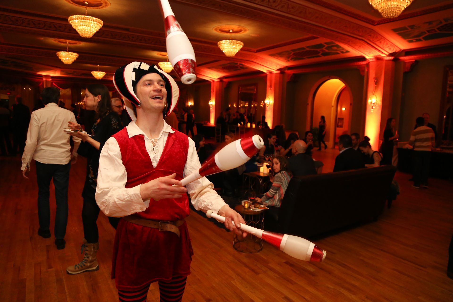 A man in a pirate costume is juggling juggling pins in a large room.