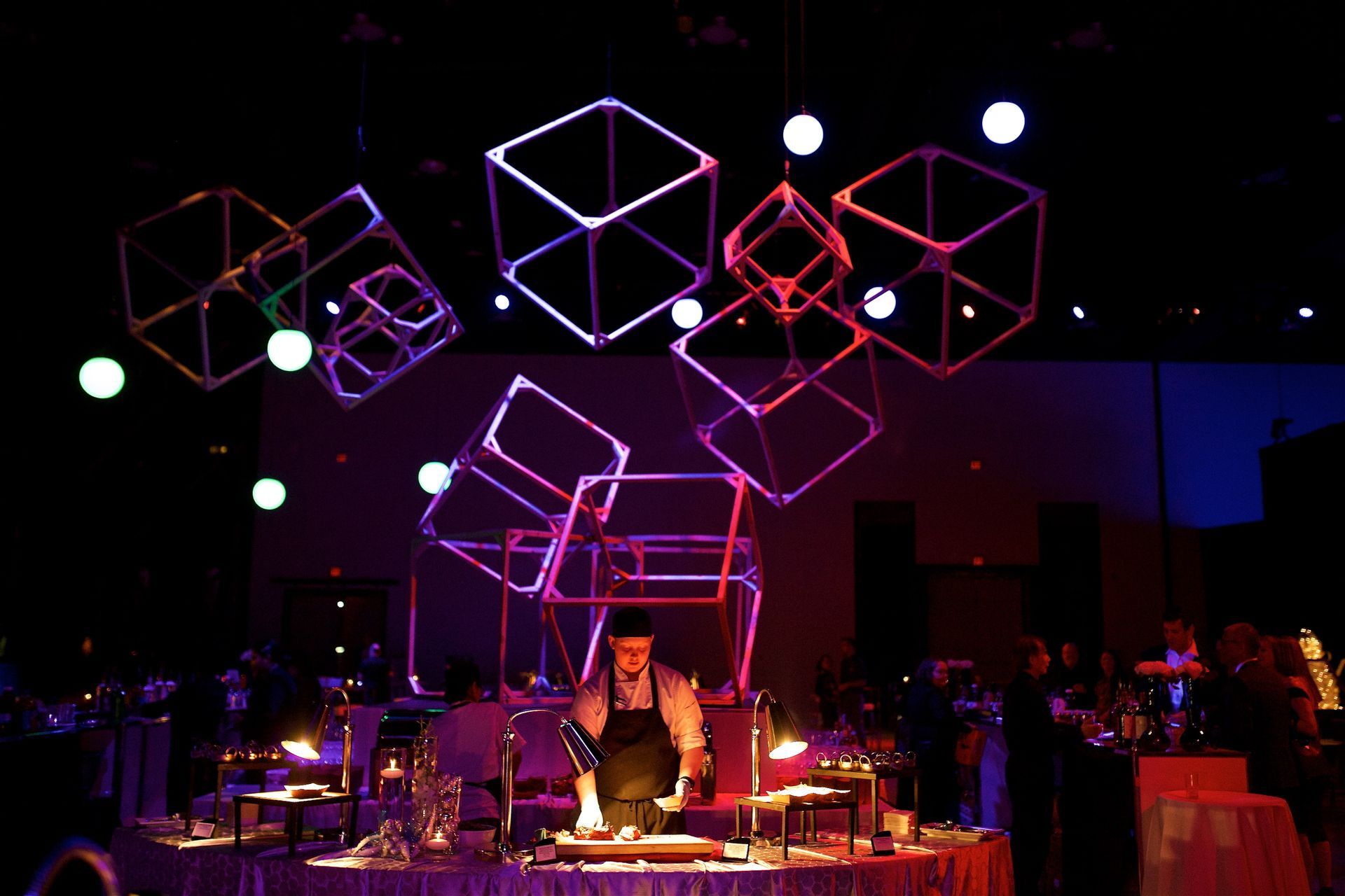 A man in an apron is cooking in a dark room with purple lights hanging from the ceiling