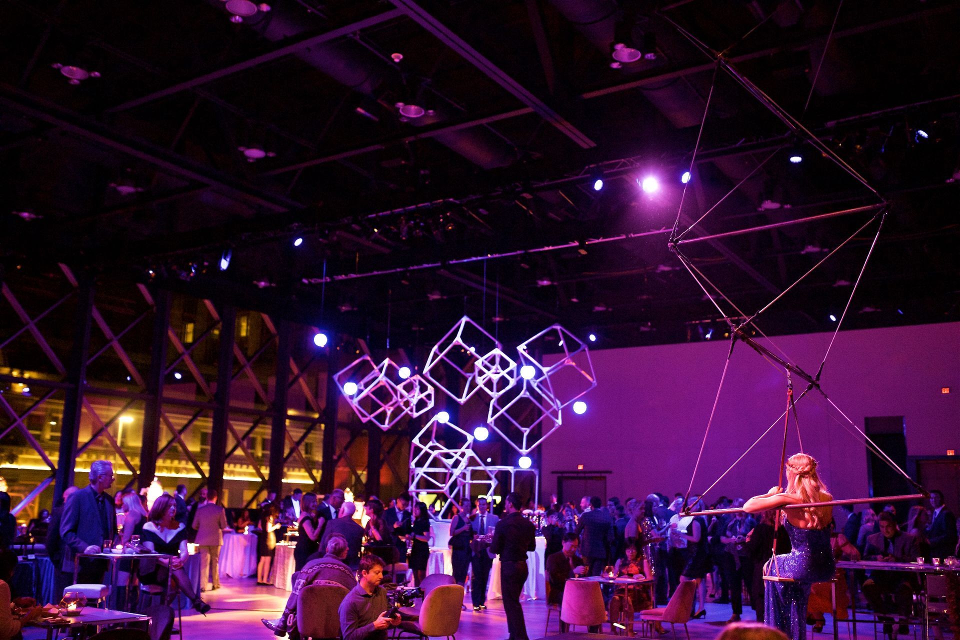 A crowd of people are gathered in a large room with purple lights