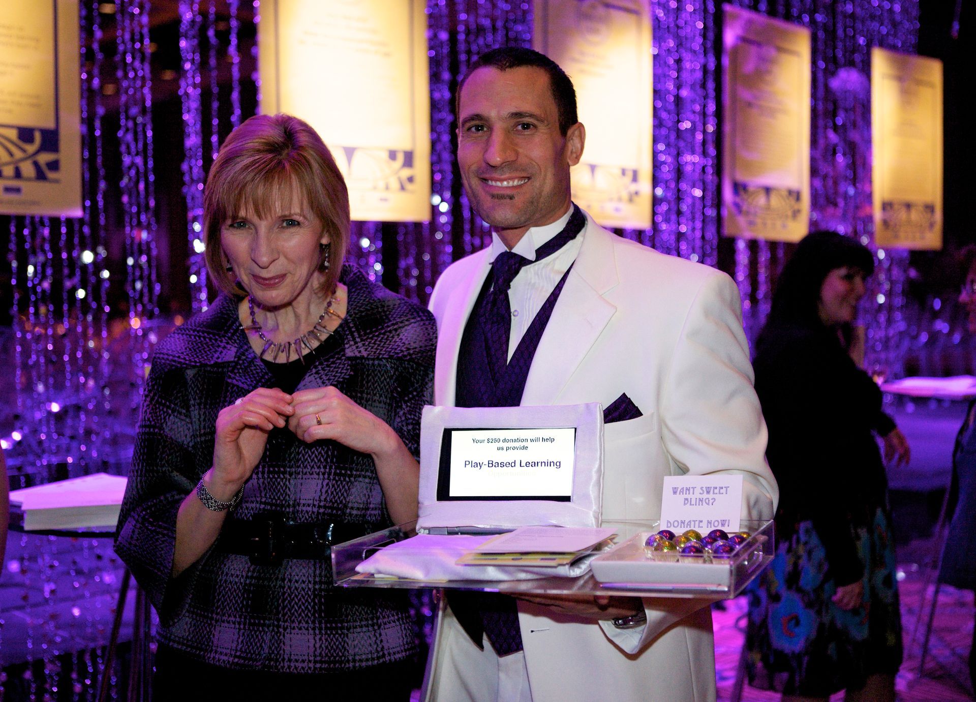 A man in a tuxedo is holding a tablet next to a woman