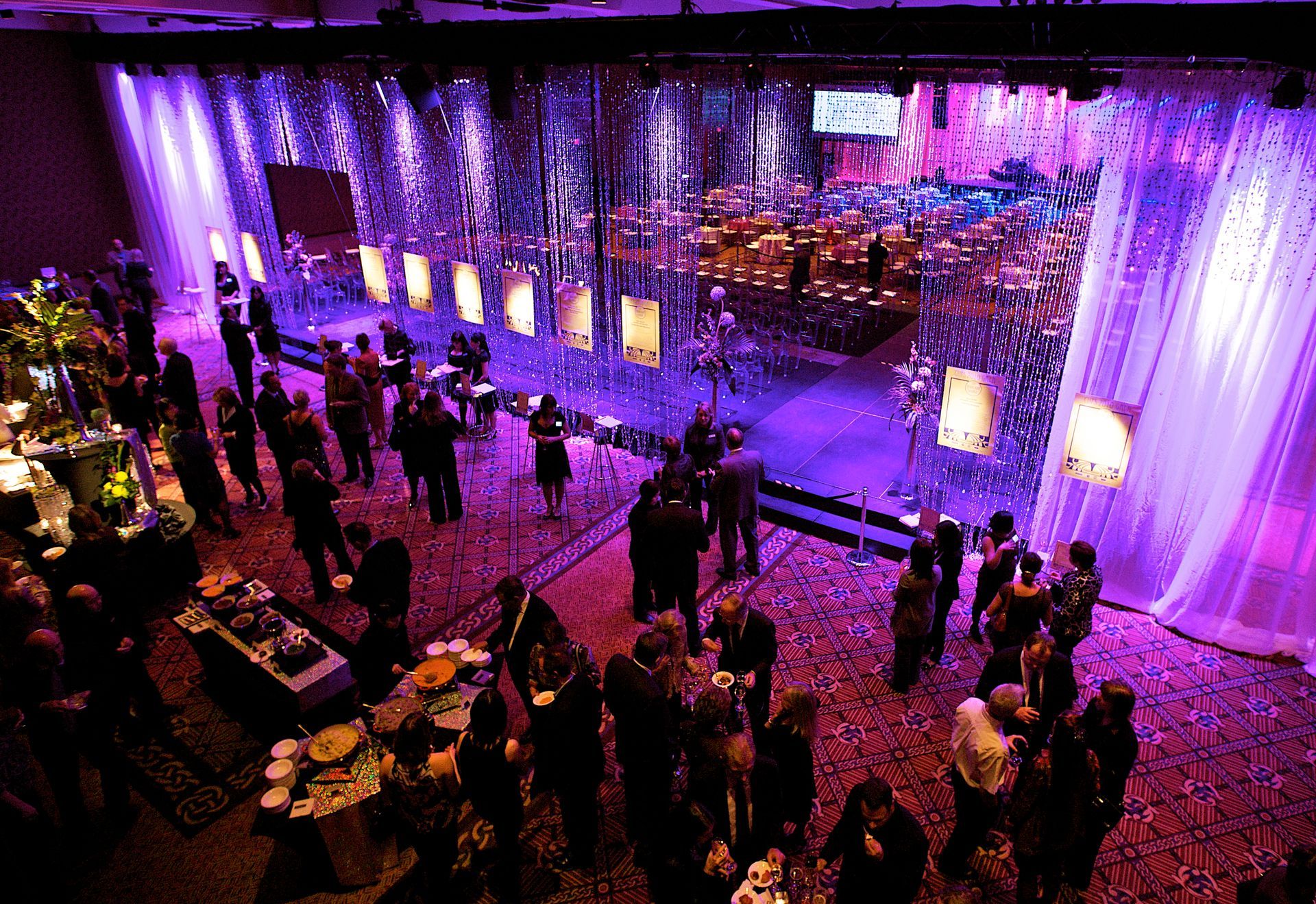 A group of people are standing in a large room with purple lights.