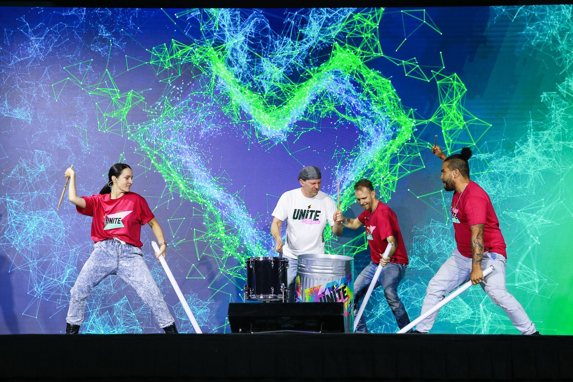 A group of people are standing on a stage holding sticks and playing drums.