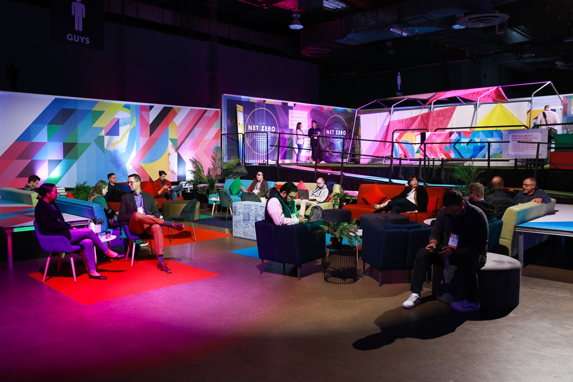 A group of people are sitting in a room with a stage in the background.