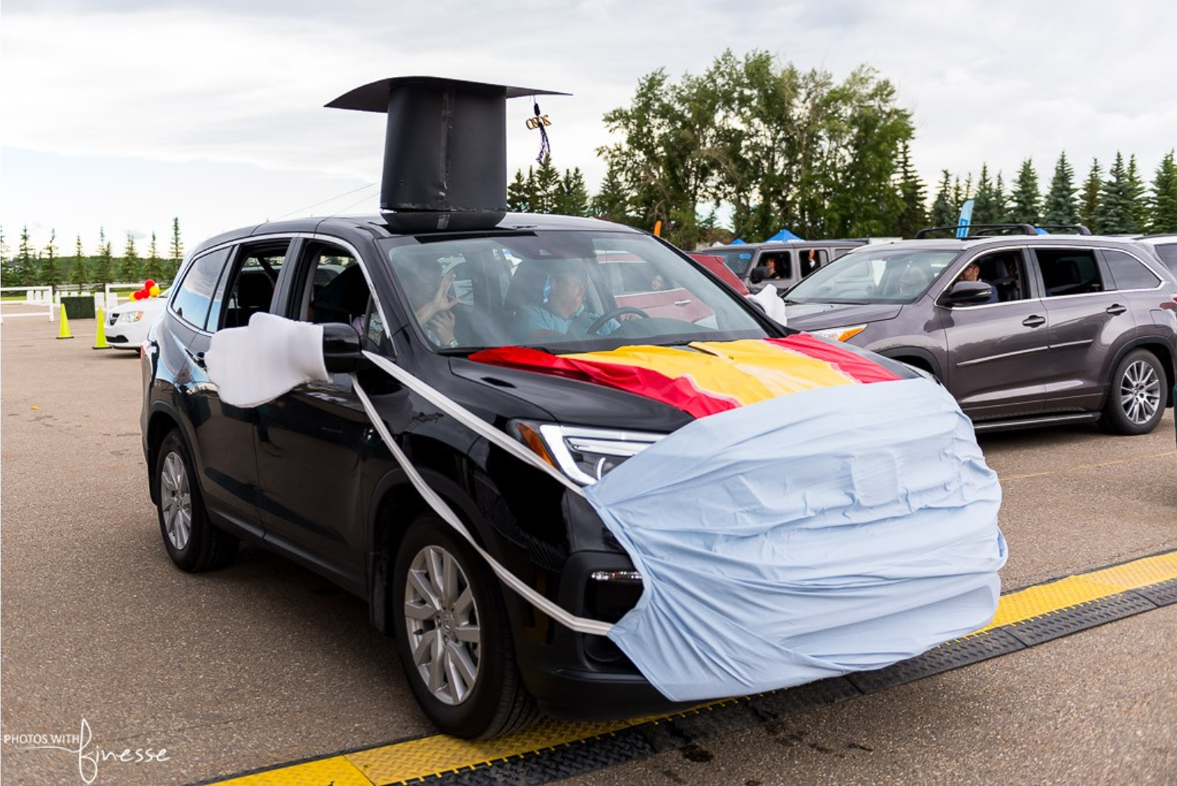 A car is decorated with a graduation cap and a medical mask.