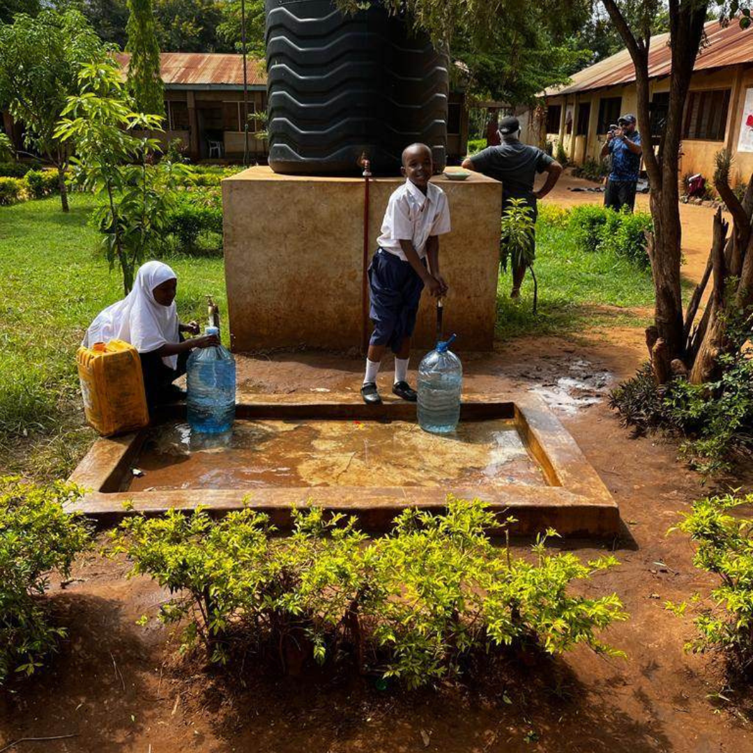 Children in Tanzania, Africa filling a bucket of water in front of a water tank