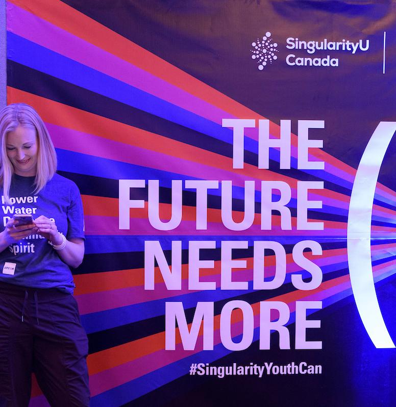 A woman stands in front of a sign that says the future needs more