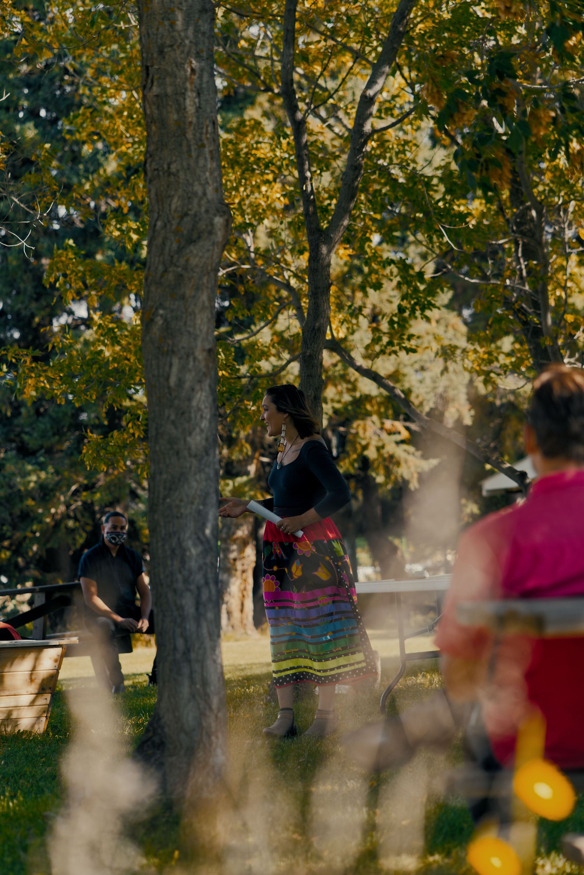 A woman is standing next to a tree in a park.