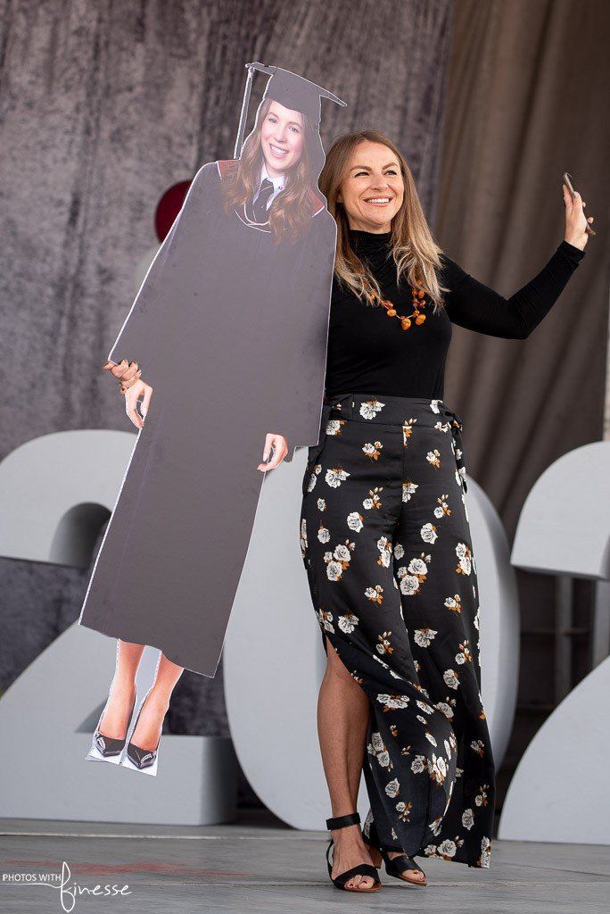 A woman is holding a cardboard cutout of herself in a graduation cap and gown.