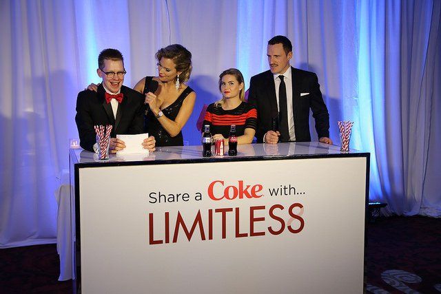 A group of people standing behind a sign that says share a coke with limitless