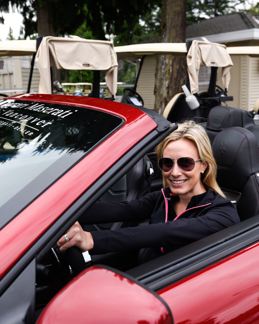 A woman wearing sunglasses is driving a red convertible car