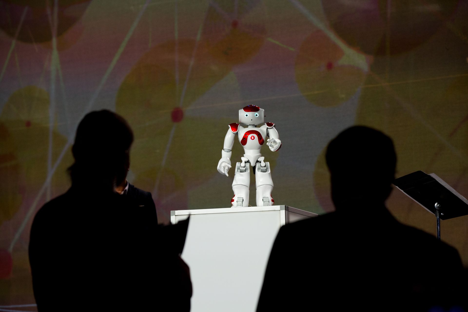 Two people are looking at a robot on a podium.