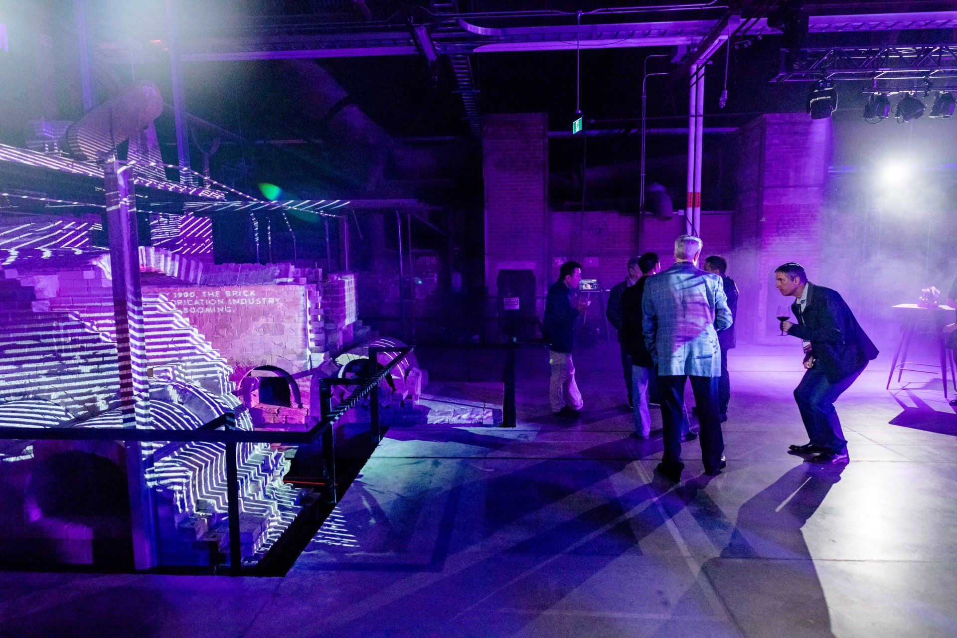 A group of people are standing in a dark room with purple lights.