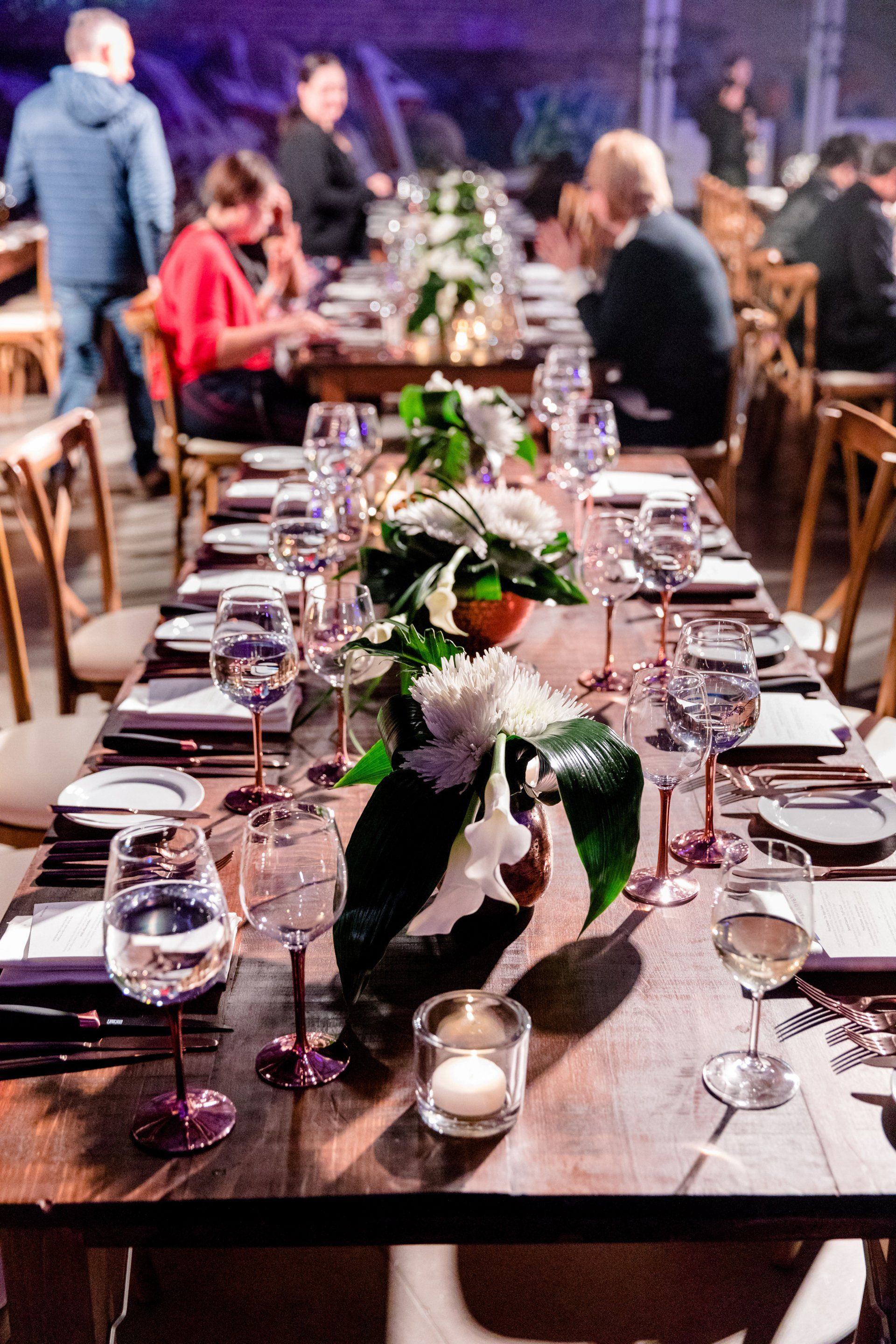 A long wooden table with plates , wine glasses , and flowers on it.