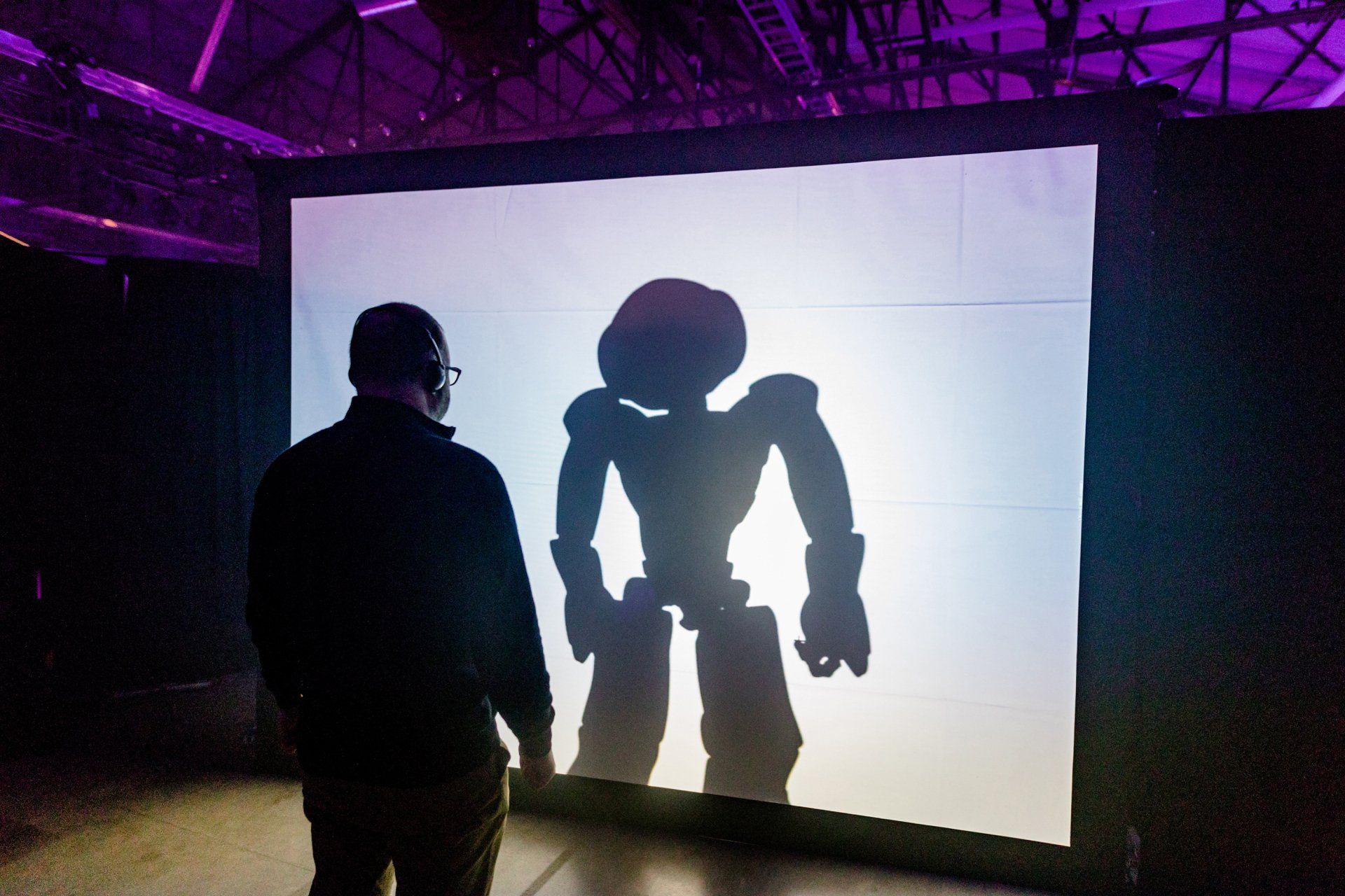 A man is looking at a shadow of a robot on a large screen
