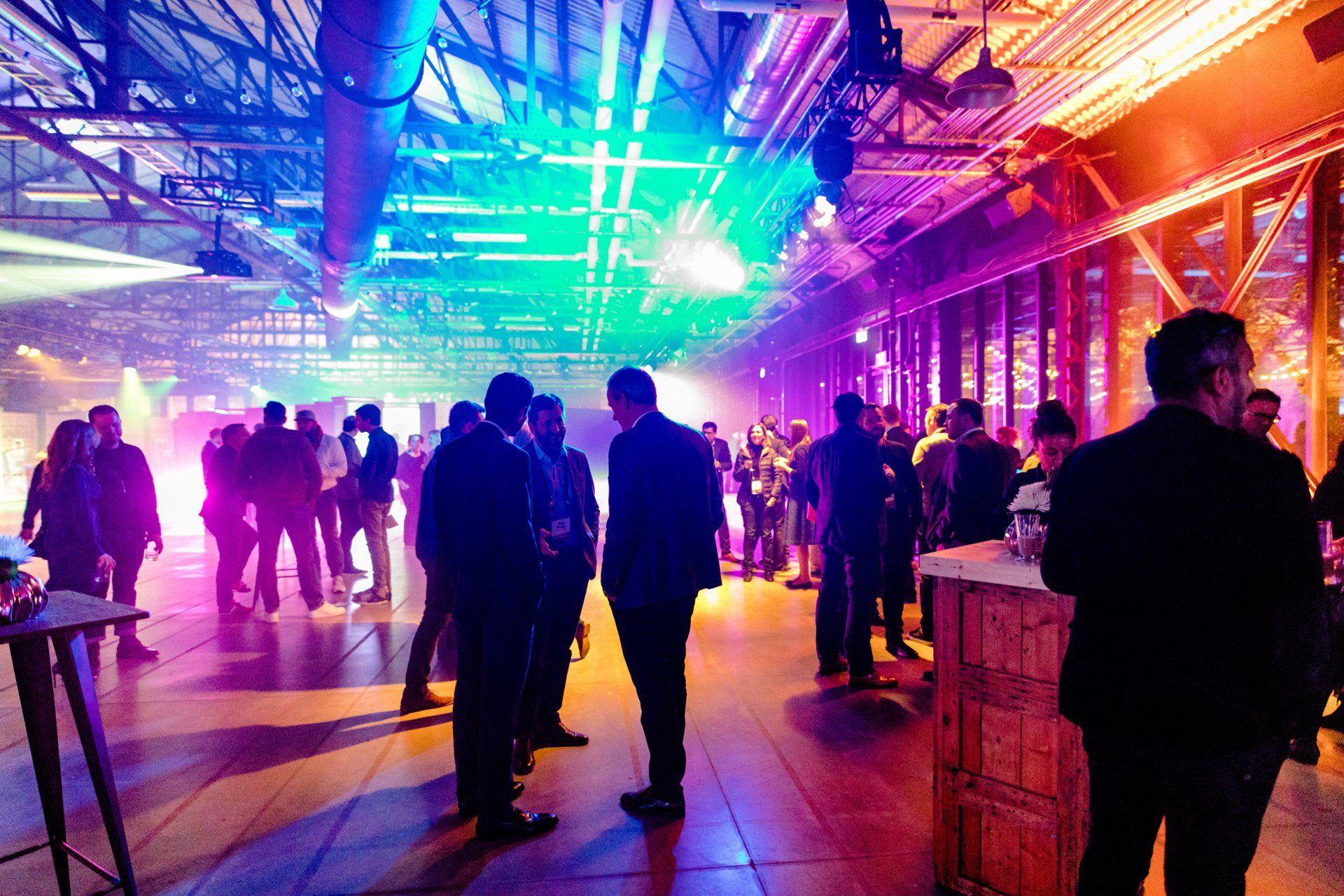 A group of people are standing in a large room with purple and blue lights.