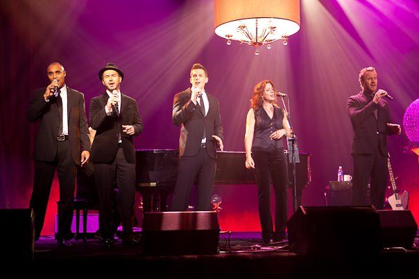 A group of people singing into microphones on a stage