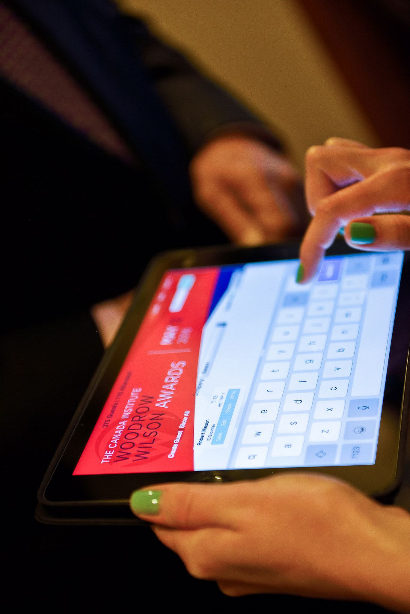 A woman with green nails is typing on a tablet