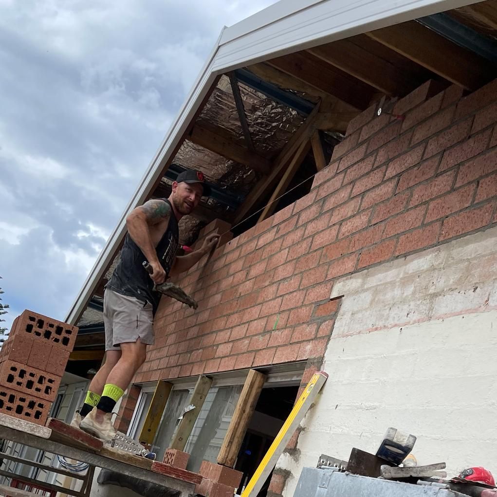 A Man Is Working On A Brick Wall With A Hammer — APEX Painting & Maintenance In Primbee, NSW