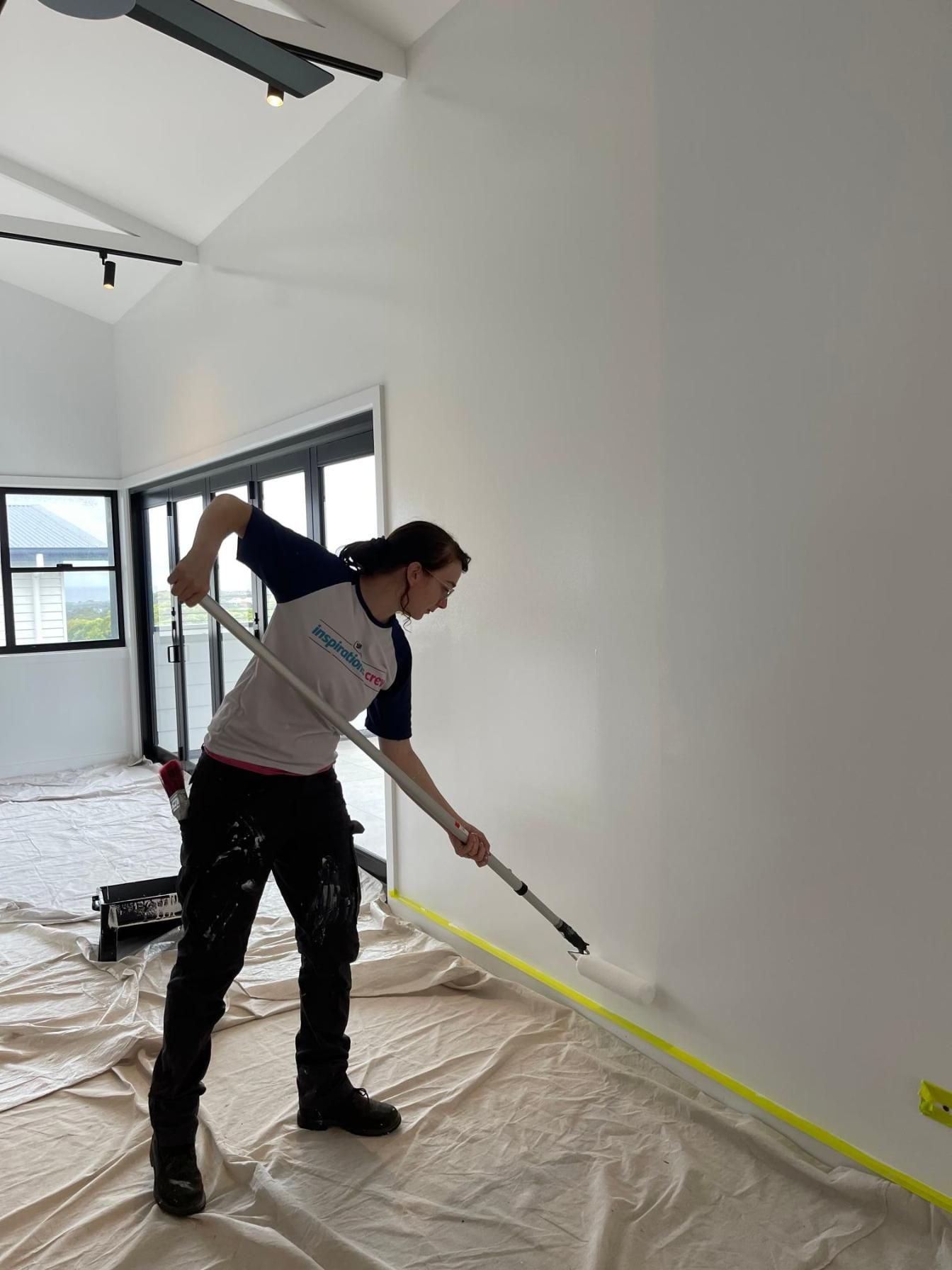 A Man Is Painting A Wall With A Roller — APEX Painting & Maintenance In Primbee, NSW