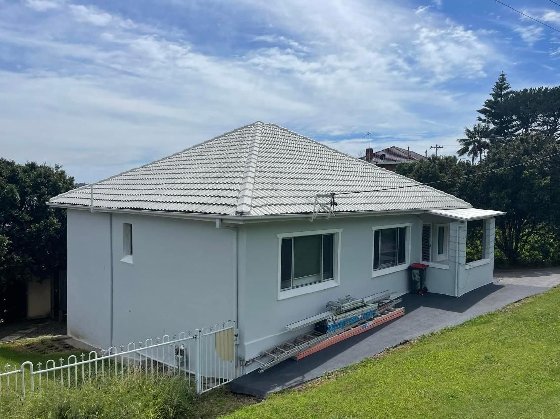 A White House With A White Roof Is Sitting On Top Of A Grassy Hill — APEX Painting & Maintenance In Primbee, NSW