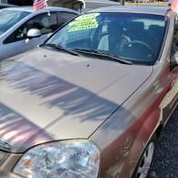 Tan car parked outdoors, viewed from the front-left side, with a windshield sale sign.