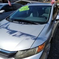 Silver sedan at a car lot with a bright green sale sign on the windshield.