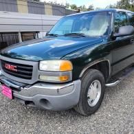 Dark green GMC pickup truck parked on gravel beside a building