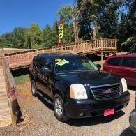 Black SUV parked outdoors beside a wooden bridge, with a red vehicle nearby and trees in the background.