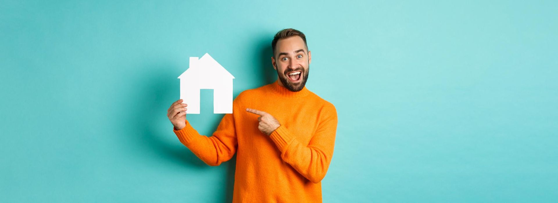 Man in orange sweater holding house cutout, pointing, and smiling against a teal background.