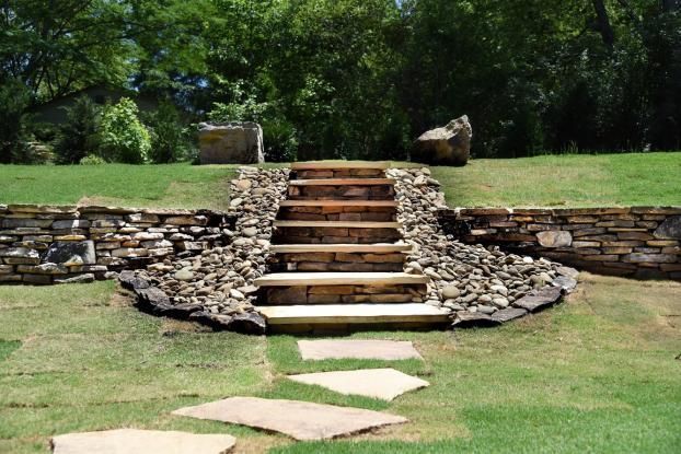 Stone steps set into a low stone retaining wall on a grassy lawn with a stone path leading up to them.