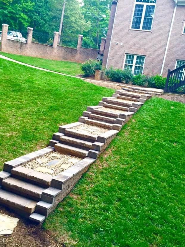 Stone steps with gravel landings lead up a grassy lawn toward a brick house.