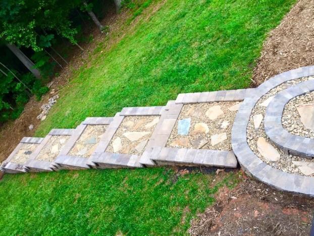 A series of stone-bordered steps filled with gravel and flagstone leading to a circular patio in a grassy yard.