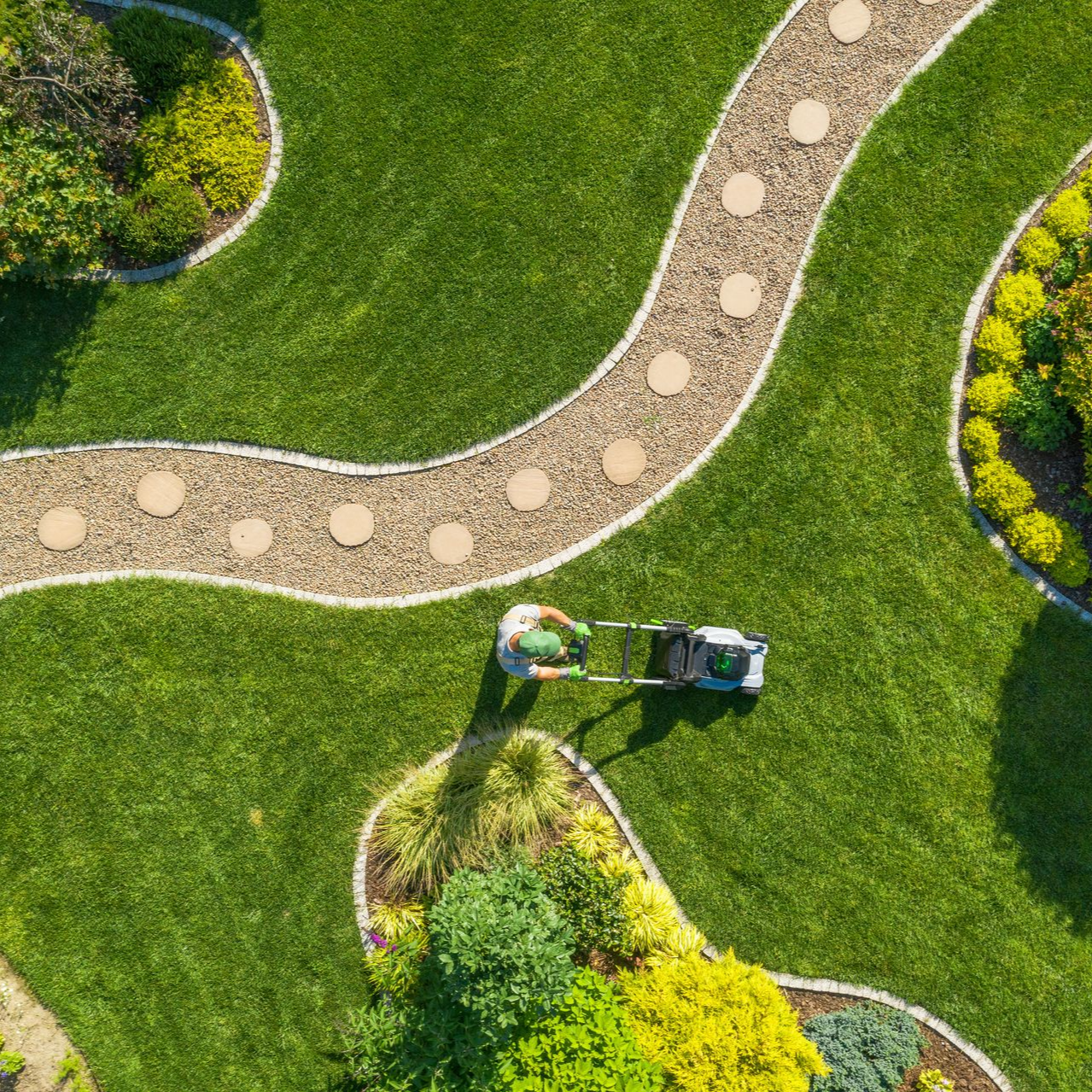 An overhead view of a person mowing a bright green lawn