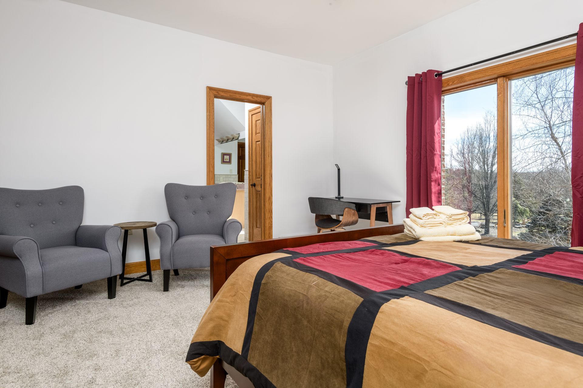 A bedroom with a bed , two chairs , a table and a large window.