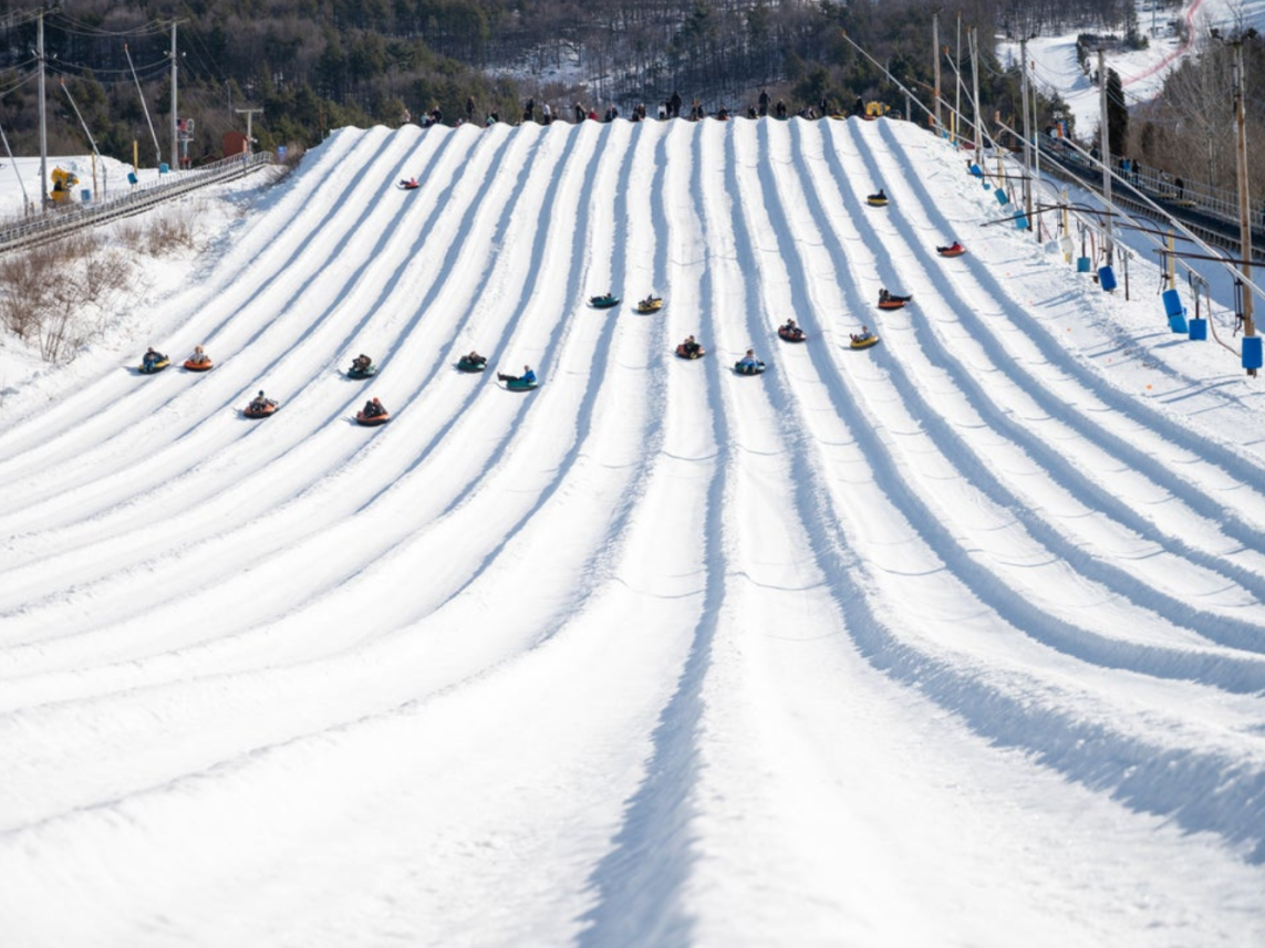A group of people are sledding down a snow covered hill.