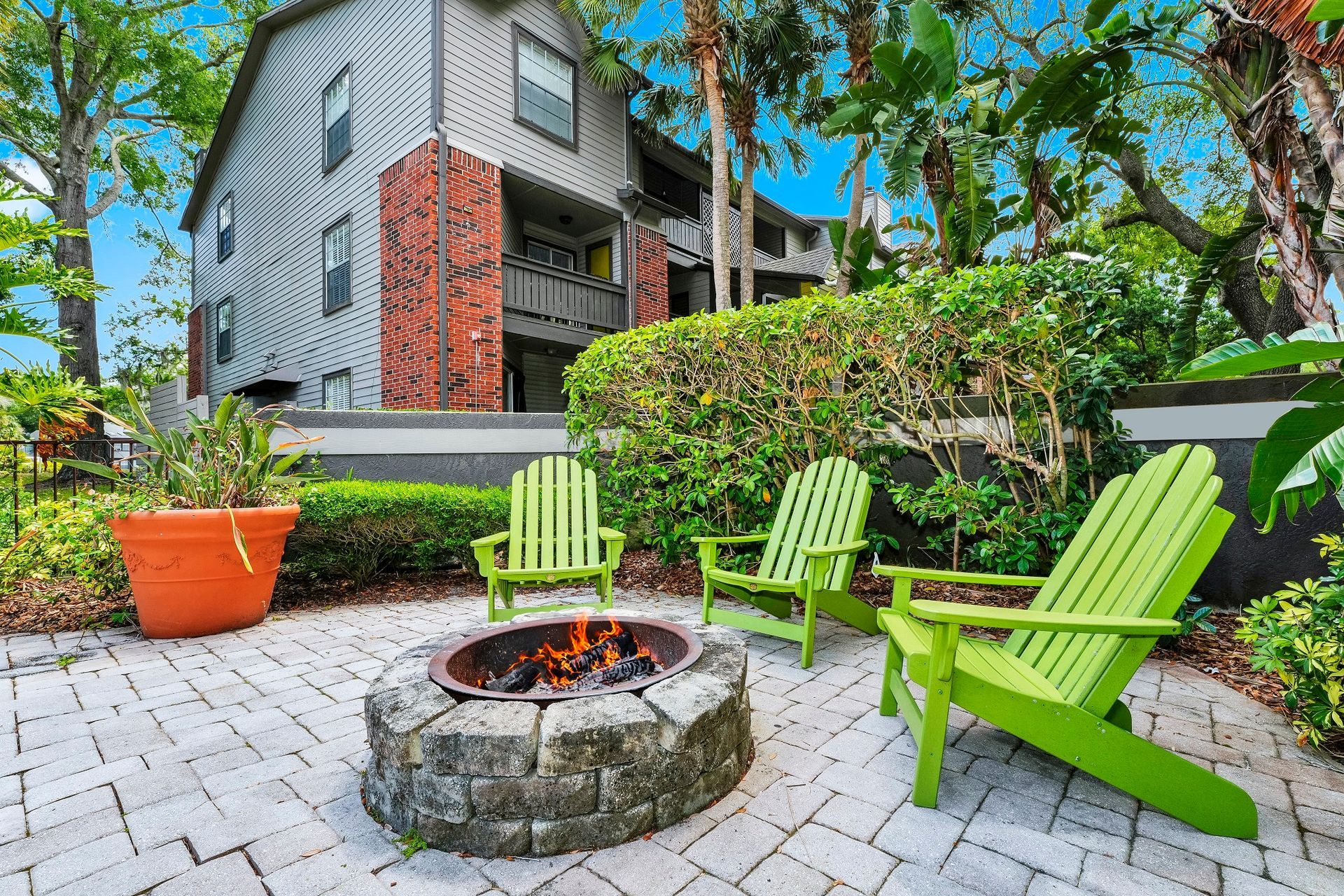 A patio with a fire pit and lime green Adirondack chairs in front of a gray and brick building.