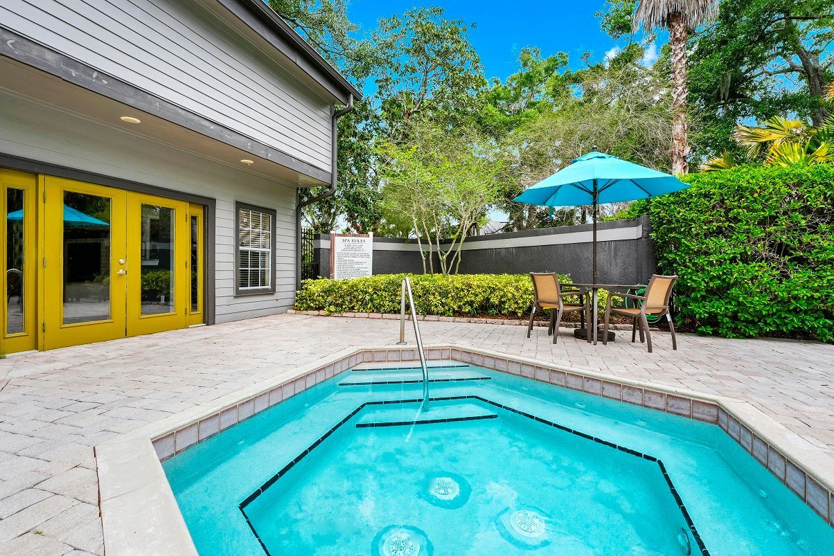Outdoor pool with turquoise water, lounge chairs, and a blue umbrella next to a building with yellow doors at The Glades in Altamonte Springs, FL..