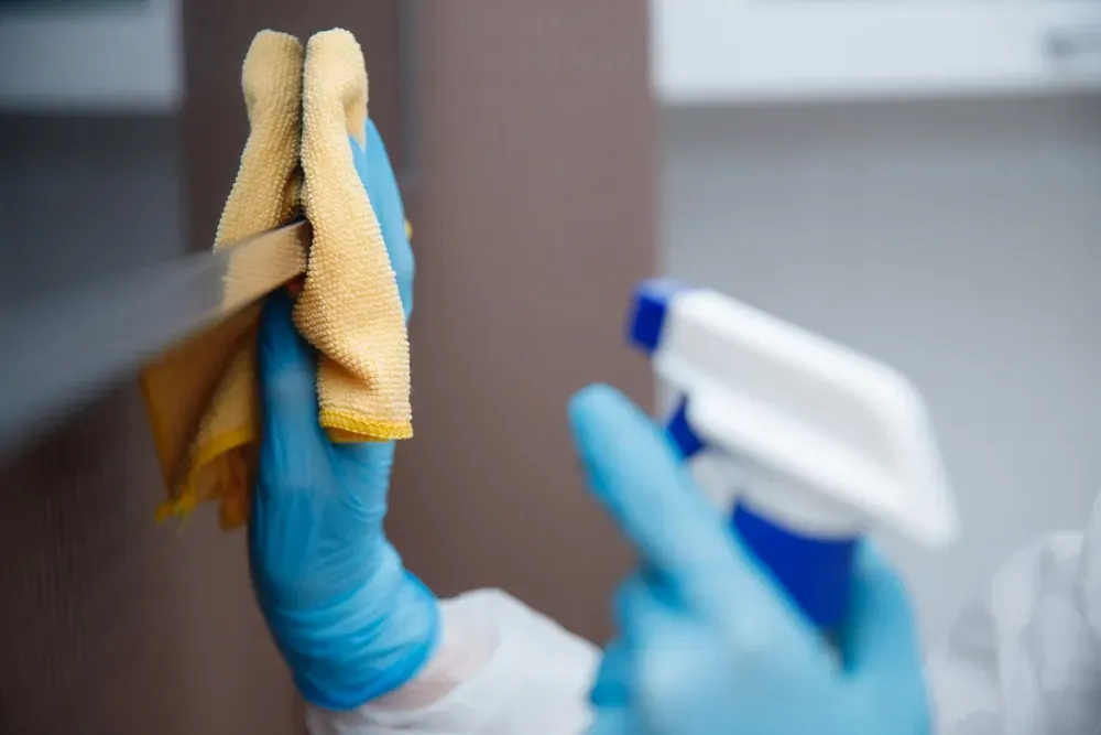 Person in blue gloves cleaning a surface with a spray bottle and yellow cloth. — Pristine Cleaning Bundaberg In Kensington, QLD