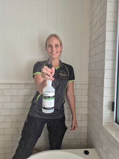 Person smiling and holding a spray bottle on a porch against a white paneled wall
