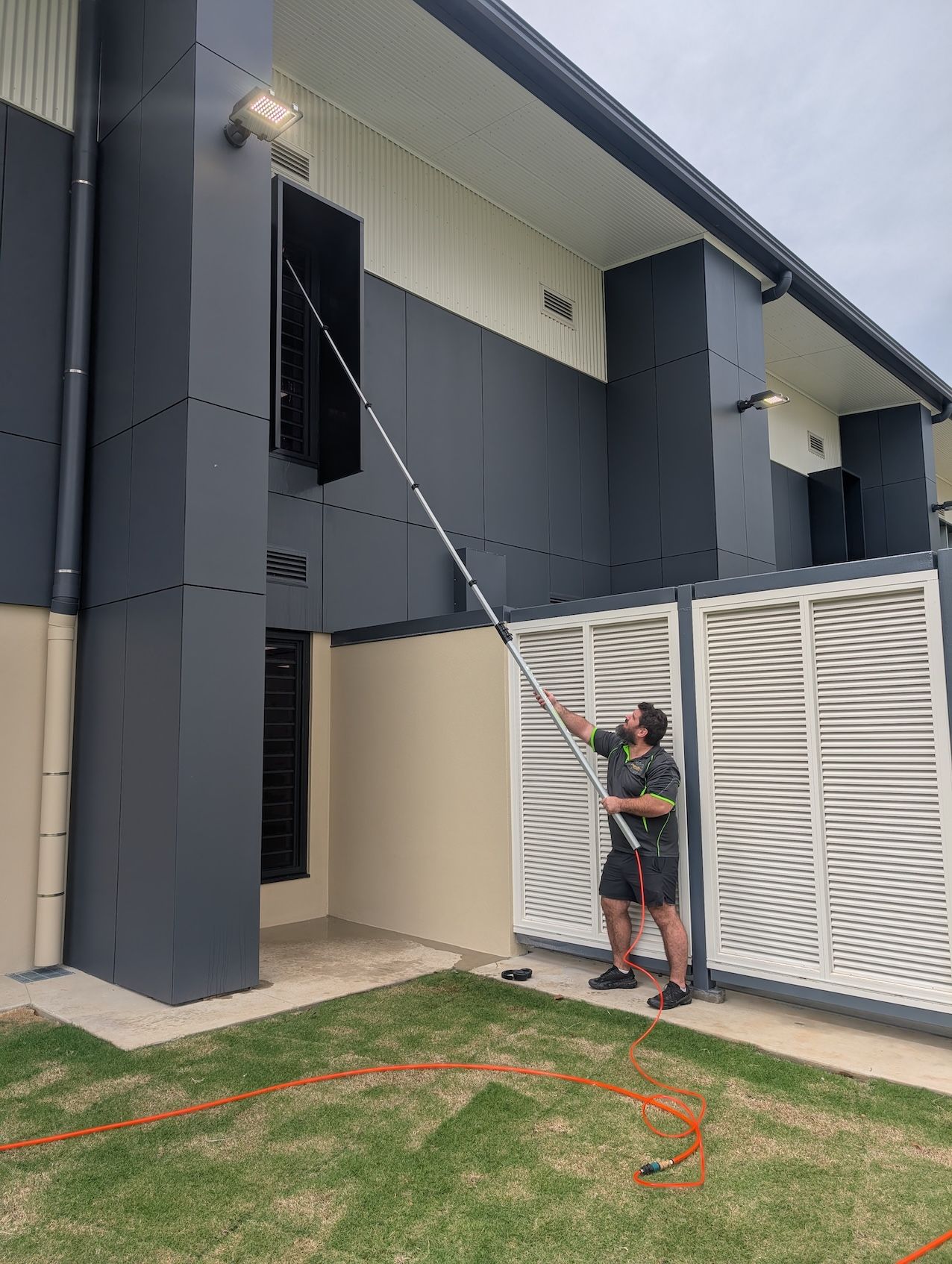 Man With Telescopic Brush Cleaning Apartment Window — Pristine Cleaning Bundaberg In Kalkie, QLD