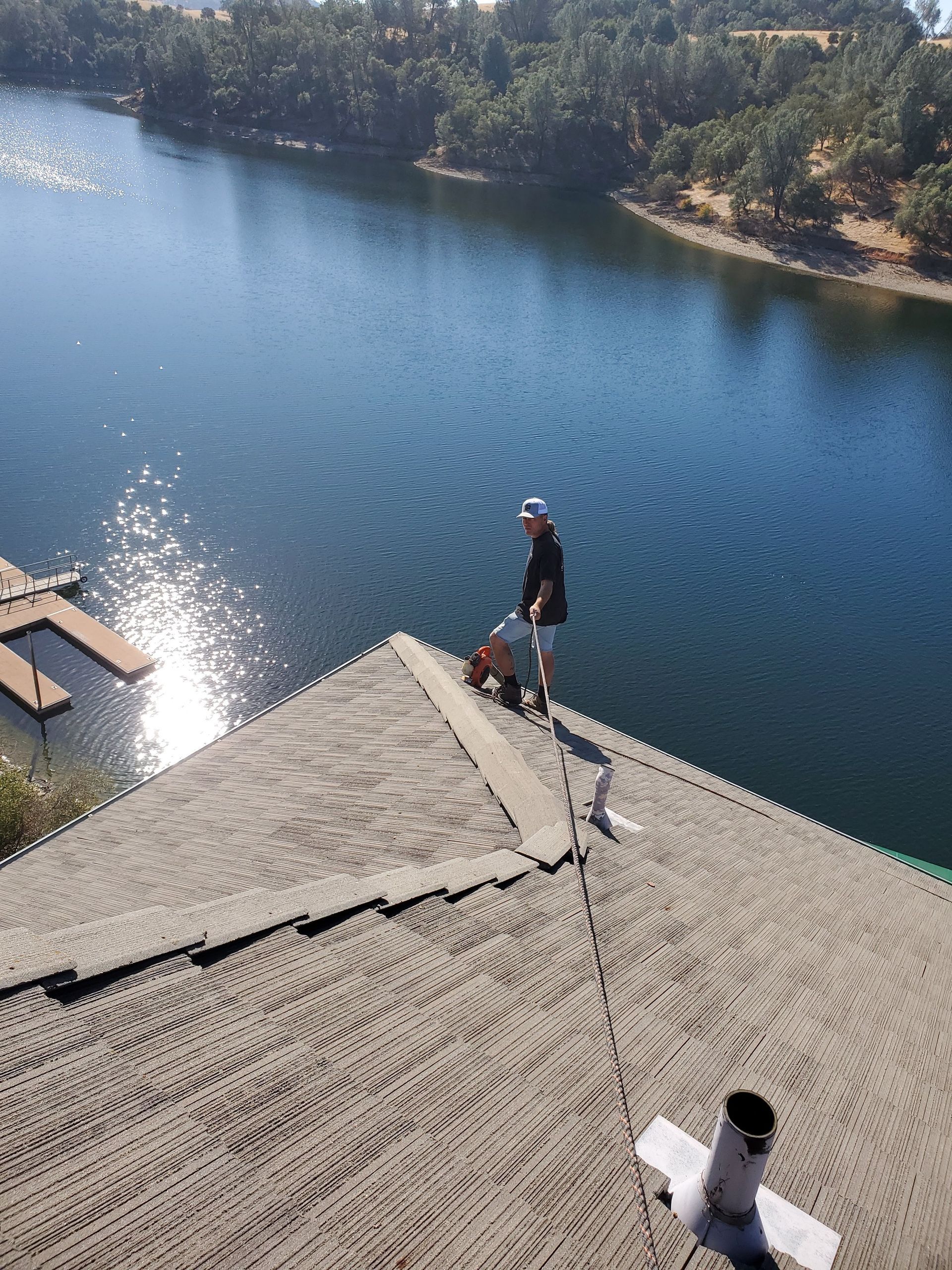 A man is standing on top of a roof overlooking a lake.