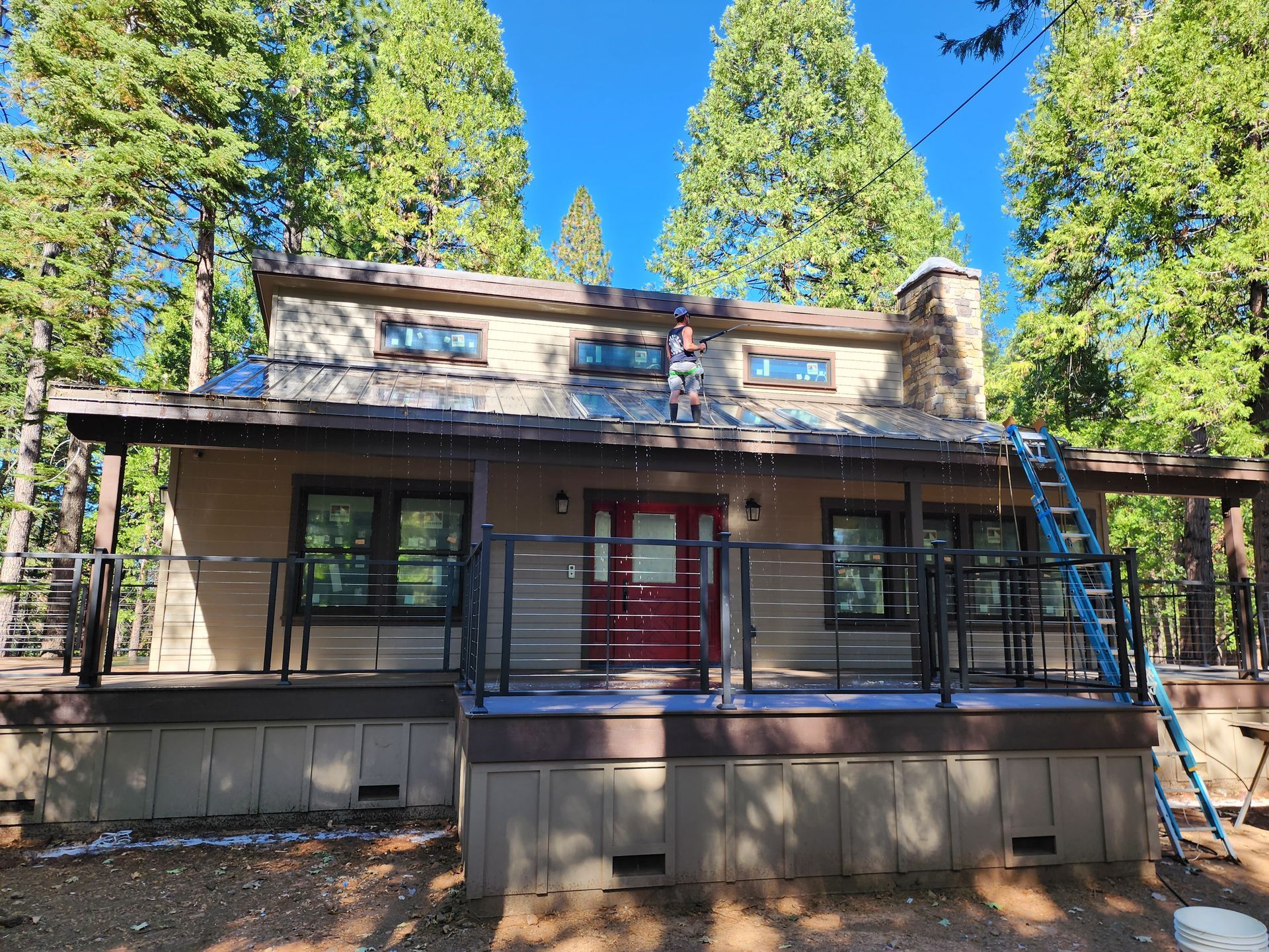 A house with a red door and a large porch is surrounded by trees.