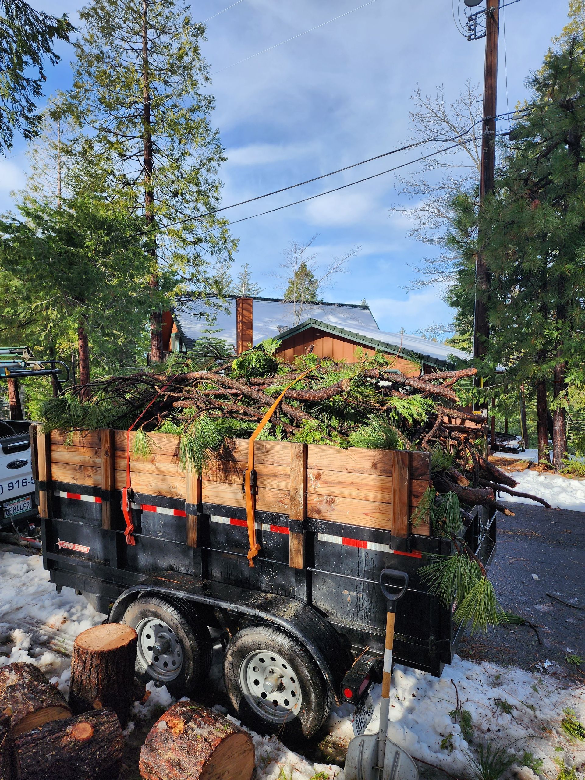 A trailer filled with logs is parked in front of a house.