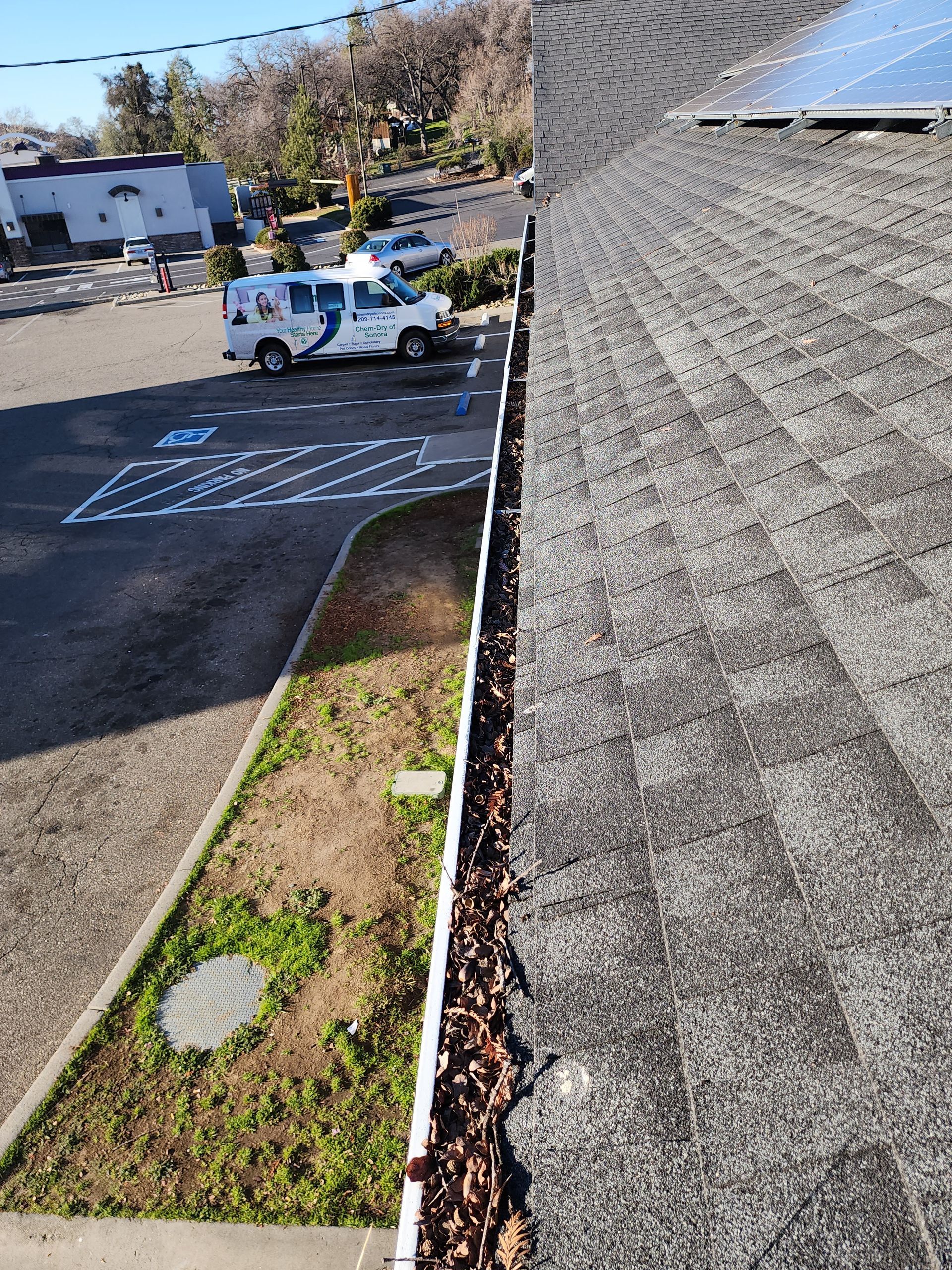 A gutter with leaves on it is sitting on top of a roof next to a parking lot.