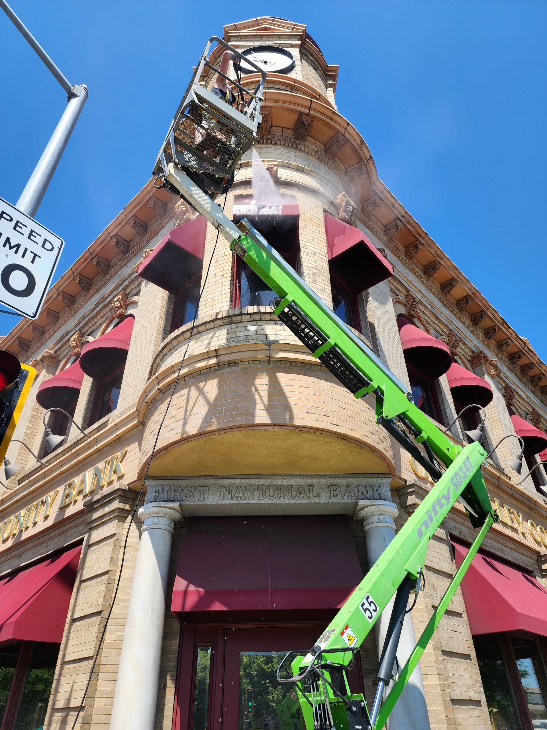 A green crane is cleaning a building with a speed limit sign in the background