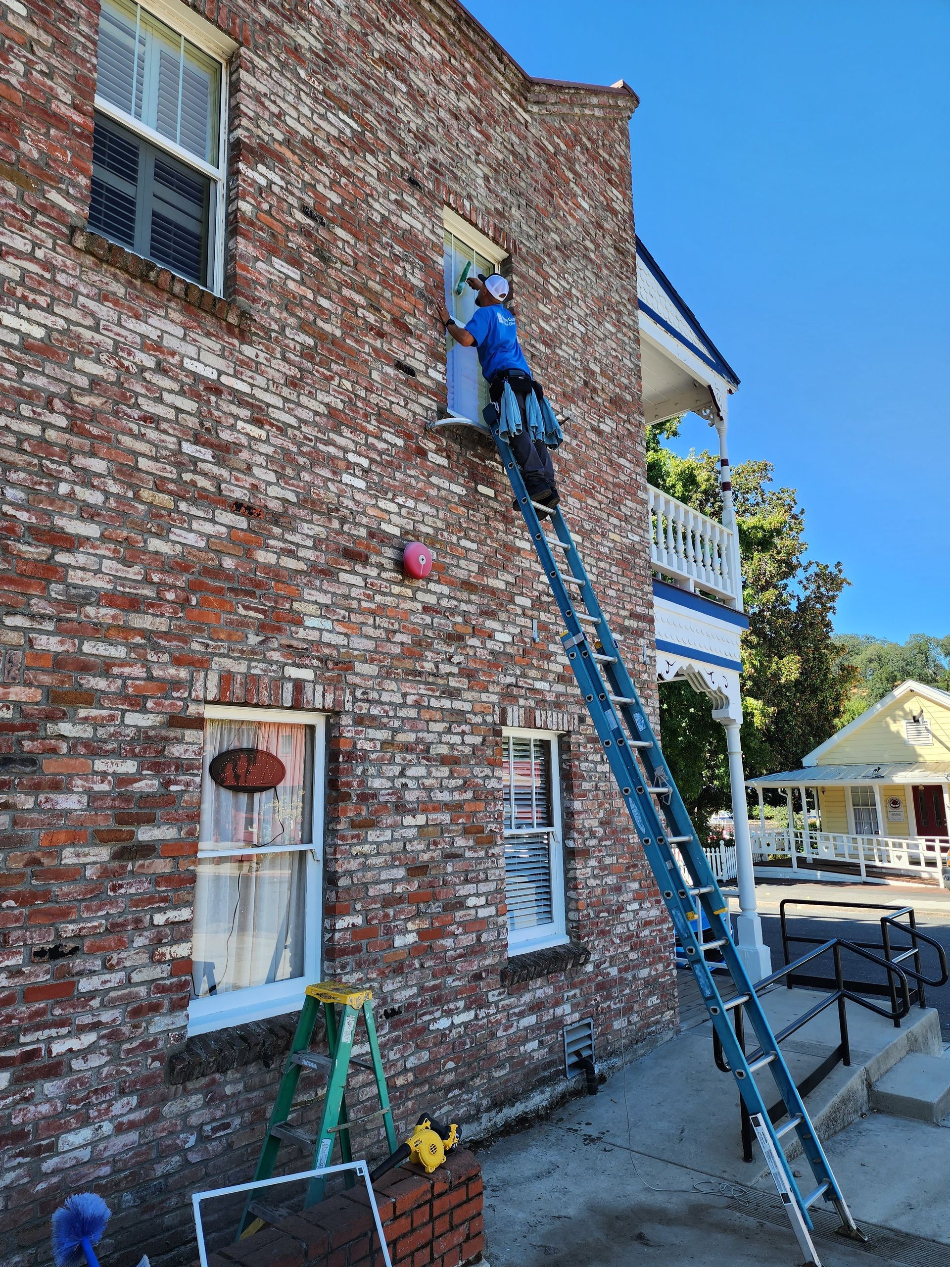A man is standing on a ladder on the side of a brick building.