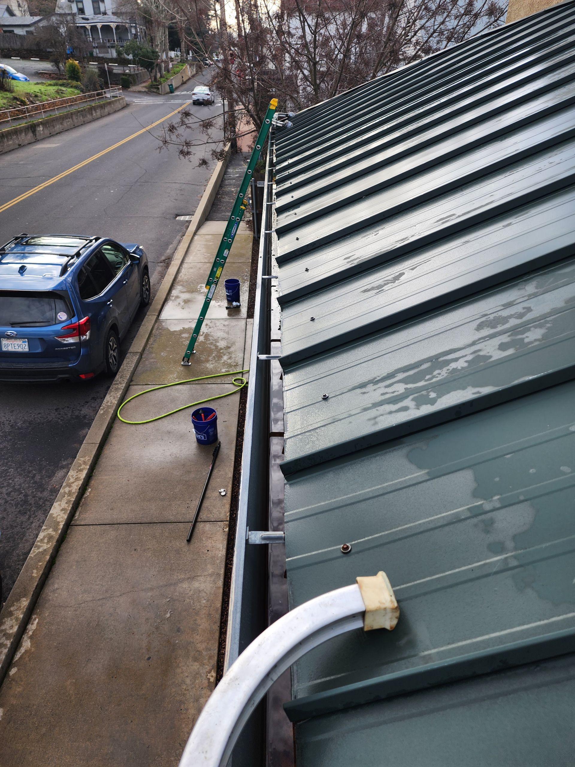 A car is parked on the side of the road next to a green roof.