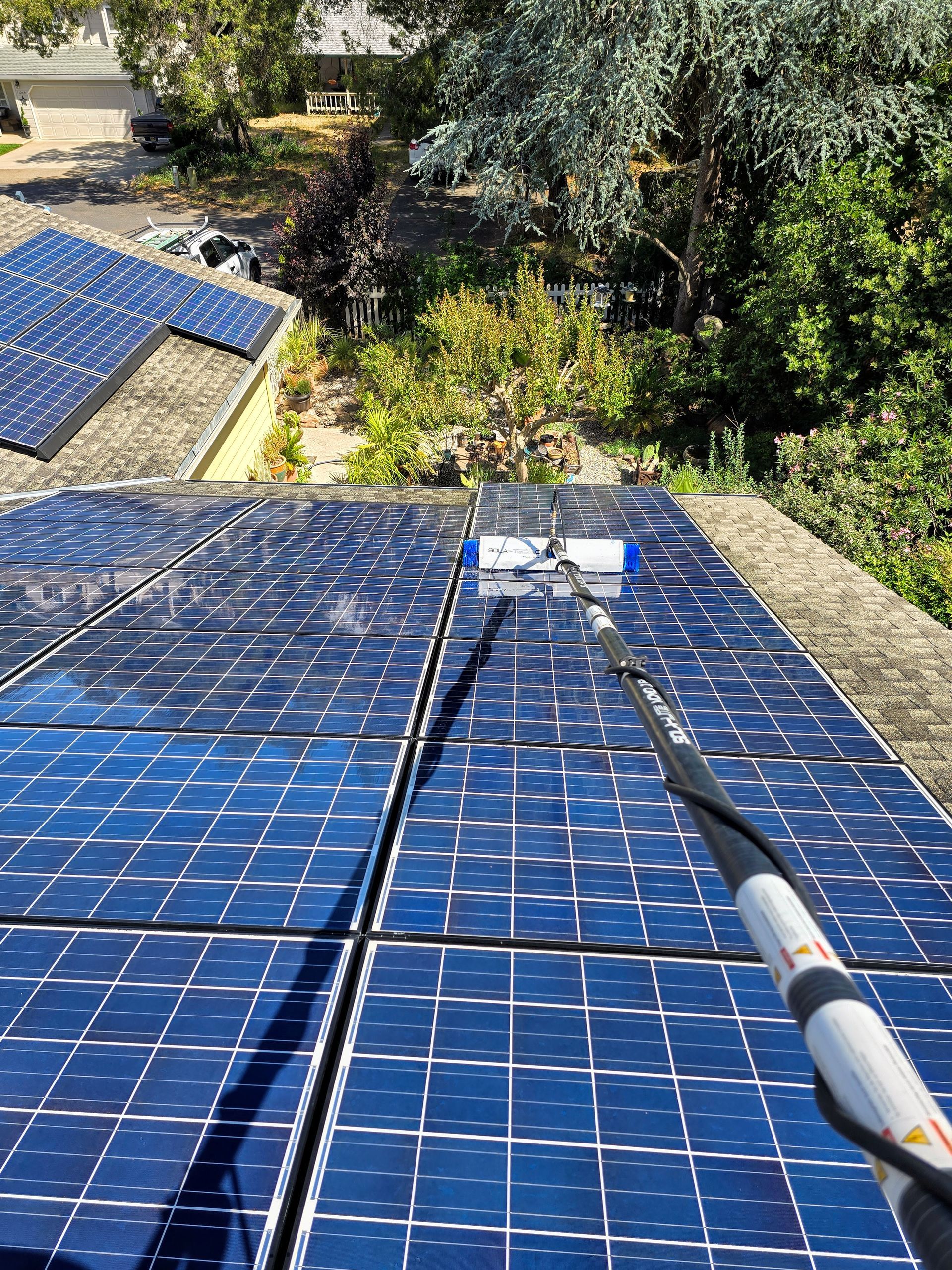 A person is cleaning solar panels on the roof of a house.