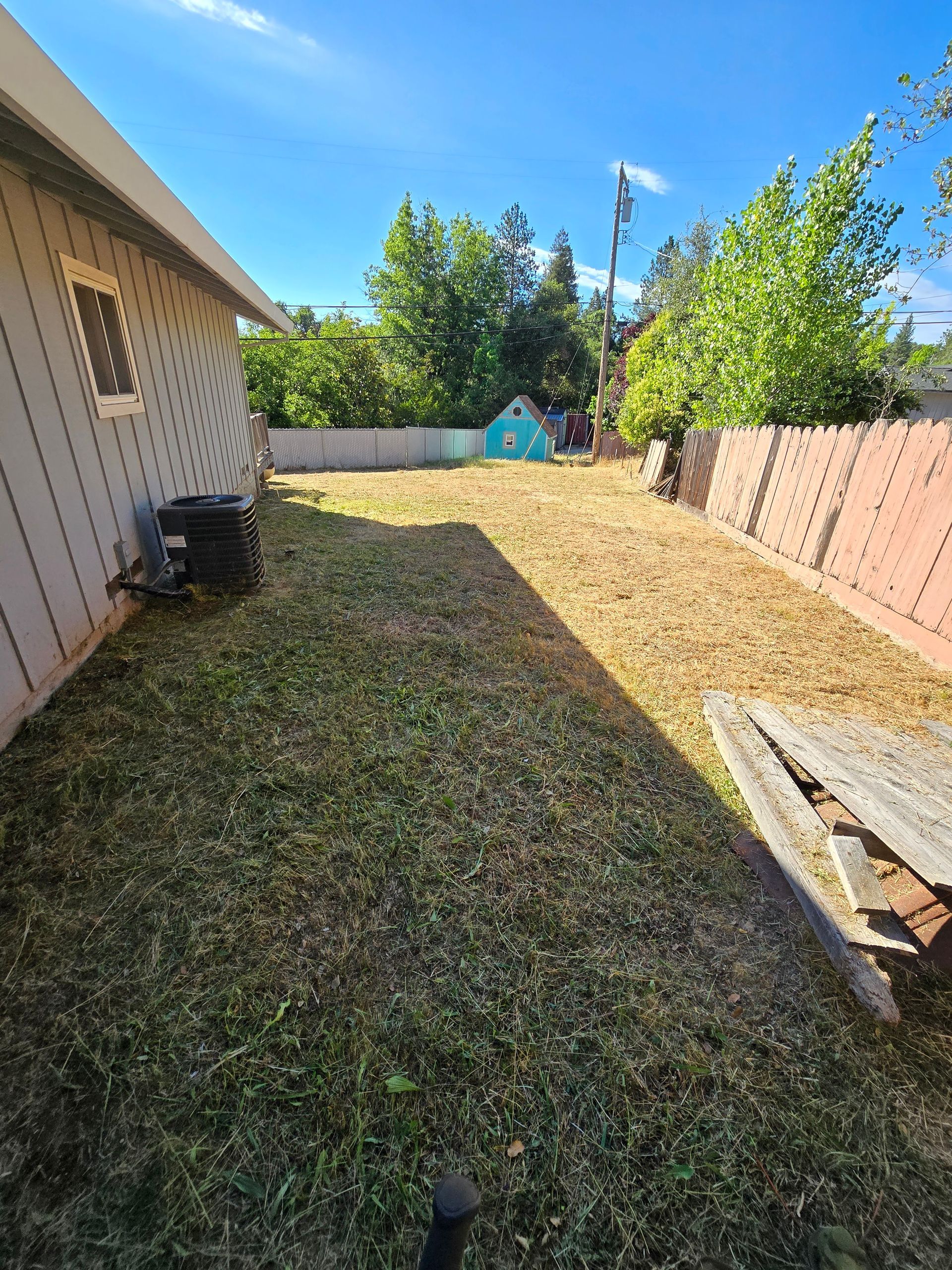 The backyard of a house with a lot of grass and a fence.
