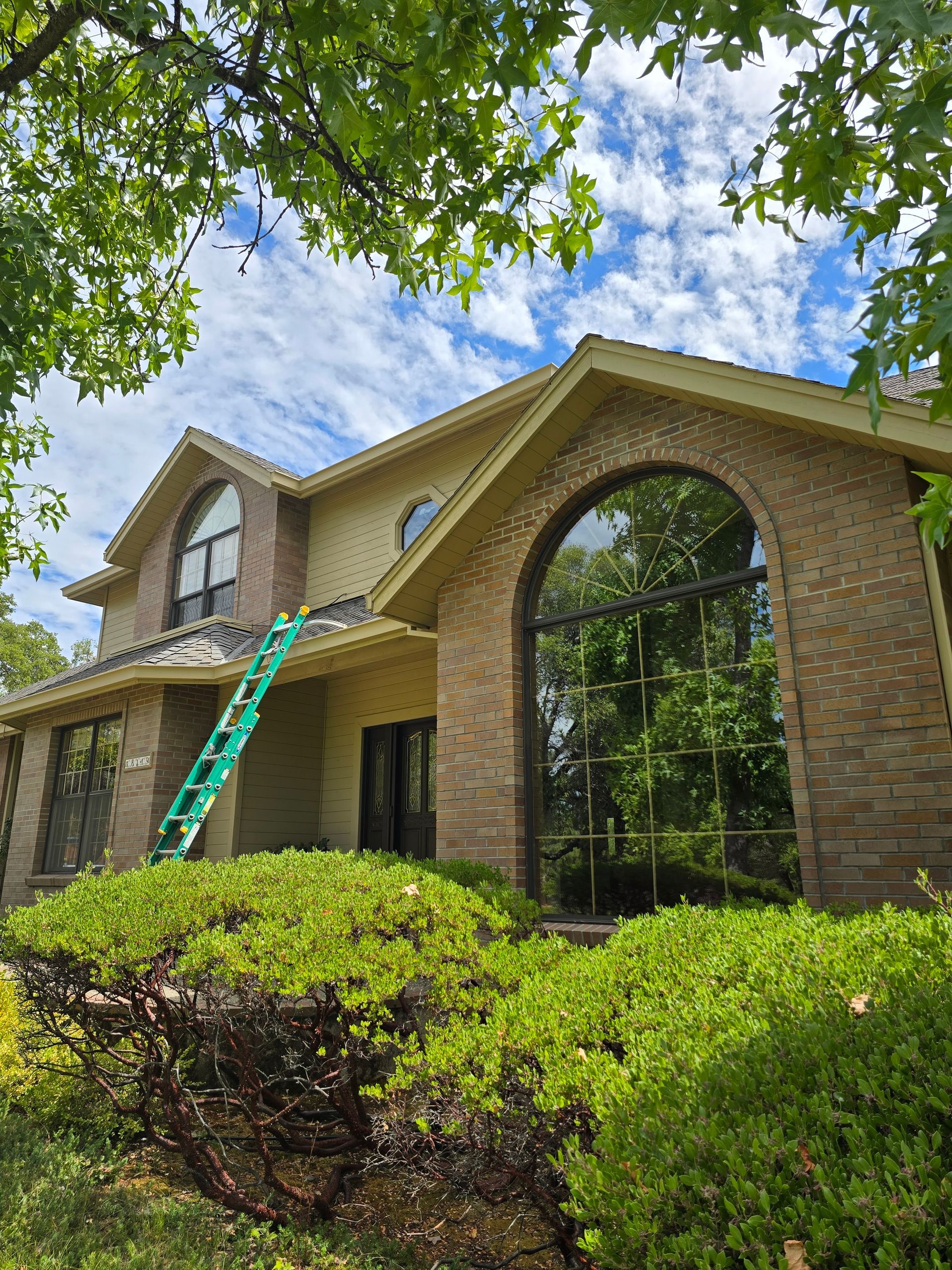 A large brick house with a green ladder on the roof.